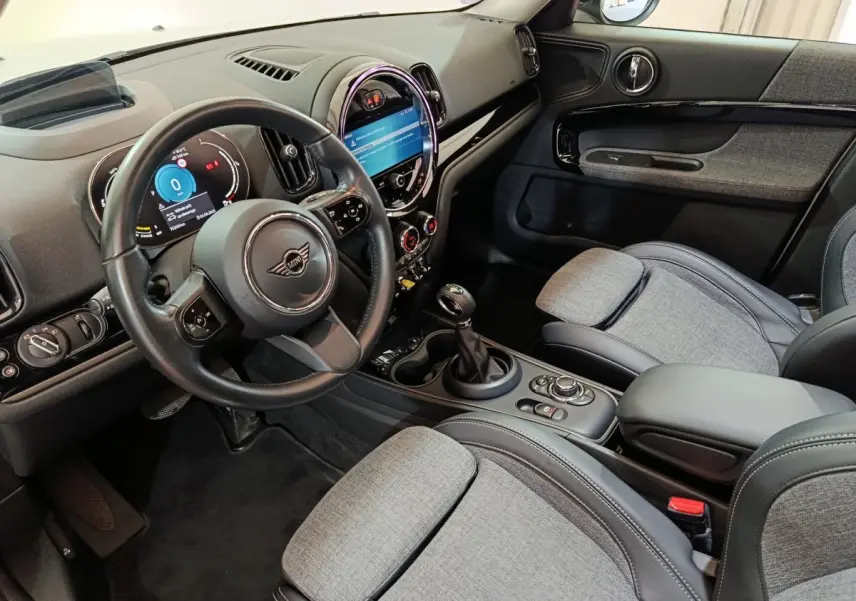 Intérieur avant droit du MINI Countryman blanc 2021, tableau de bord avec écran tactile rond et sièges gris tissu et cuir.