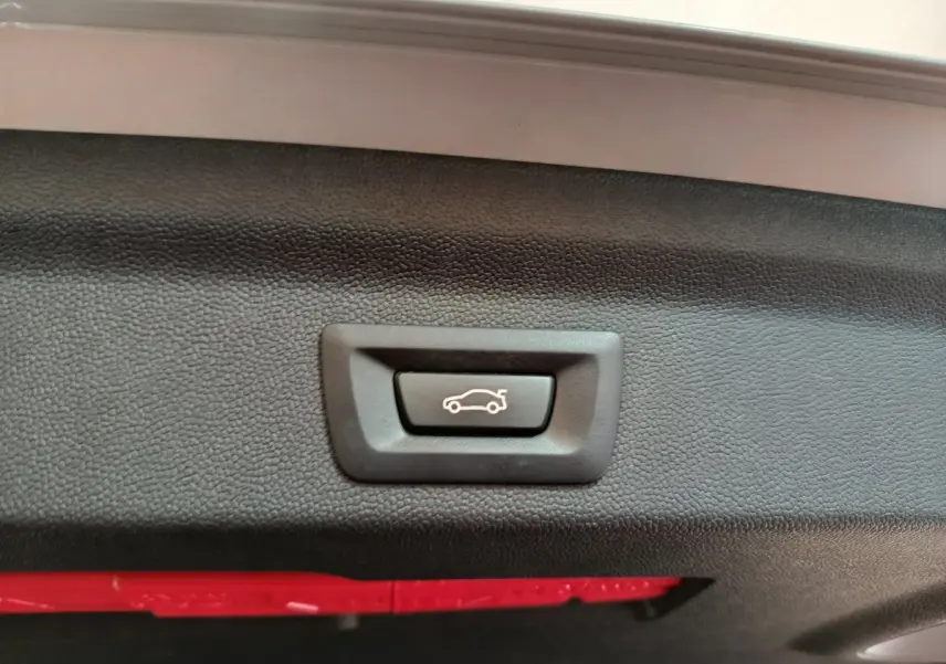 Bouton d'ouverture électrique du coffre sur la trappe intérieure d'un MINI Countryman blanc, vue rapprochée.