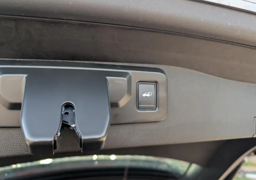 Détail du bouton d'ouverture électrique du hayon sur le bord intérieur du coffre du Renault Austral gris métallisé.