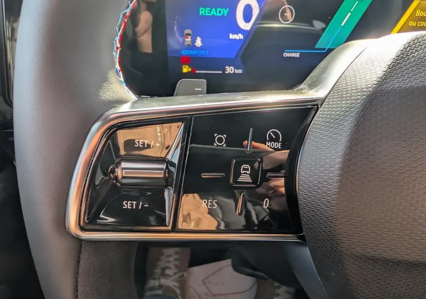 Gros plan sur les commandes au volant côté gauche du Renault Austral gris métallisé, avec affichage numérique en arrière-plan.