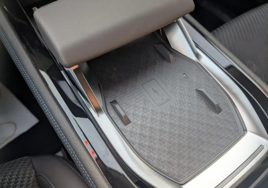 Vue rapprochée du chargeur smartphone à induction noir avec surpiqûres bleues sur la console centrale du Renault Austral gris métallisé.