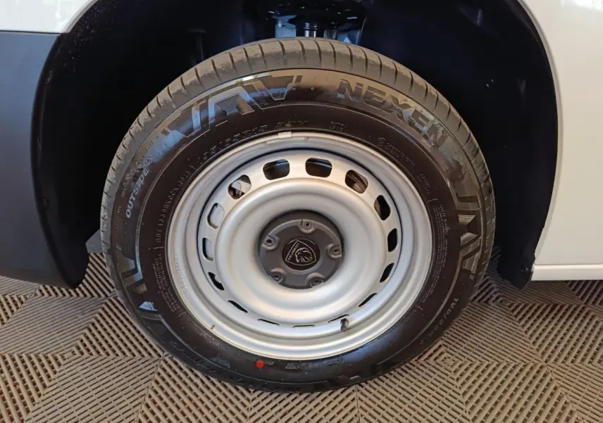 Gros plan sur la roue avant droite en acier gris du Peugeot Partner blanc, avec logo Peugeot au centre.