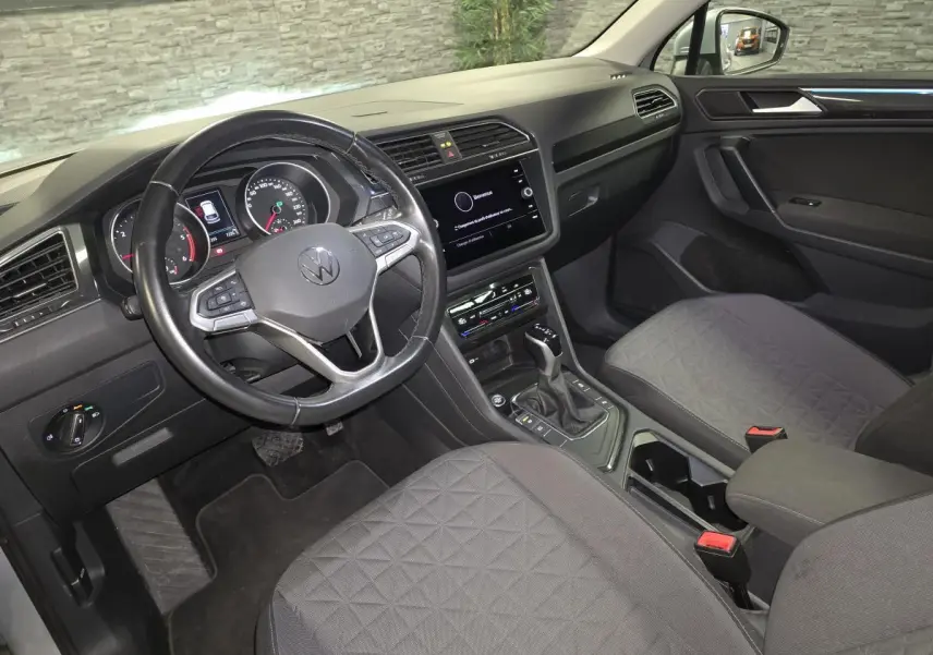 Vue intérieure avant droite du Volkswagen Tiguan 2023, sellerie tissu gris avec volant multifonctions cuir et écran tactile central.