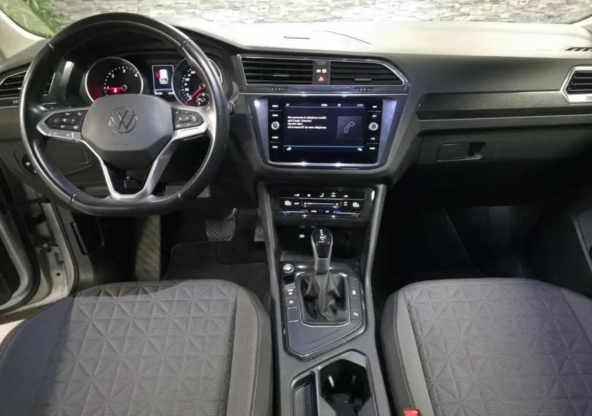 Vue intérieure avant du Volkswagen Tiguan 2023 gris, montrant volant cuir multifonctions et écran tactile central.