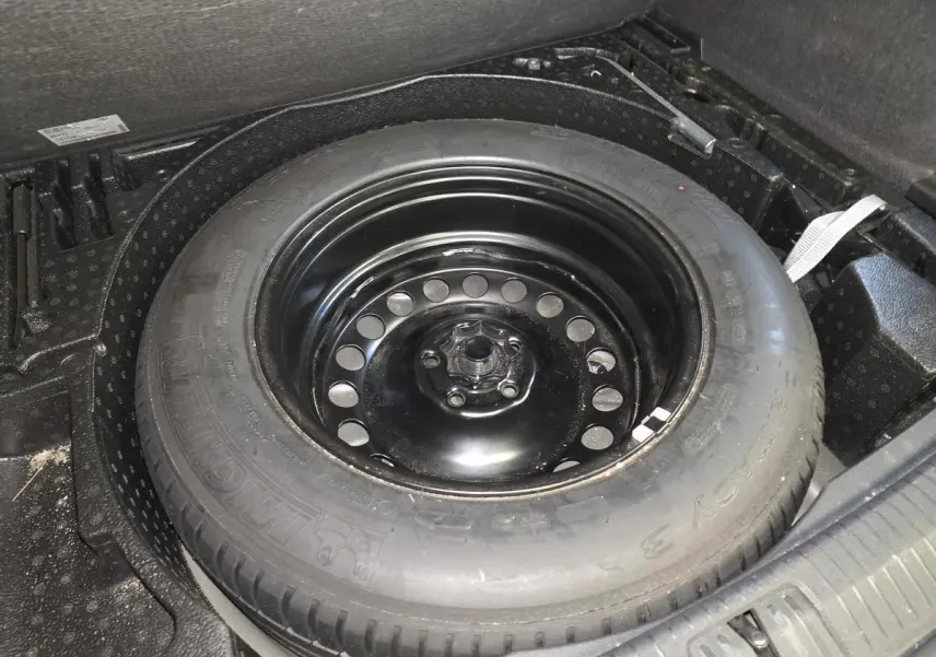 Gros plan sur la roue de secours en acier noir dans le coffre du Volkswagen Tiguan gris 2023.