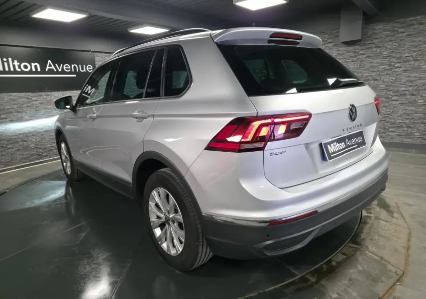 Volkswagen Tiguan gris métallisé vu en 3/4 arrière droit, feux arrière LED allumés, jantes alliage 17 pouces.