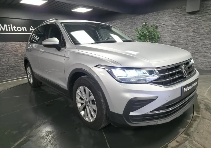 Volkswagen Tiguan gris métallisé en 3/4 avant droit avec feux LED allumés dans un showroom.