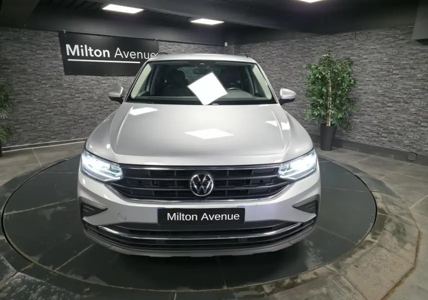 Vue avant d'un Volkswagen Tiguan gris métallisé 2023 avec phares LED allumés en showroom.