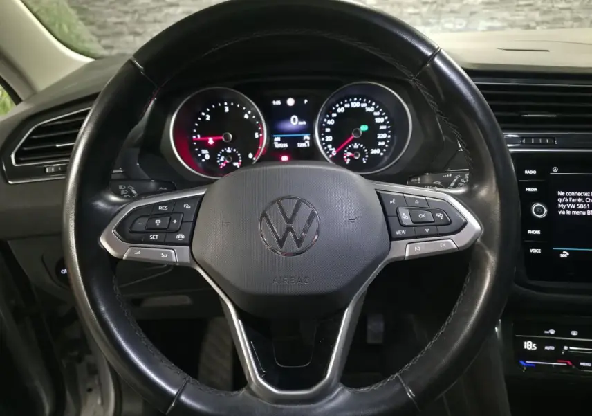 Vue rapprochée du volant cuir noir multifonctions d’un Volkswagen Tiguan 2023 avec tableau de bord et écran tactile visibles.