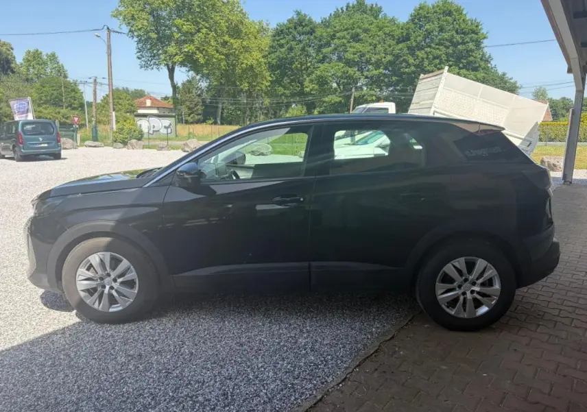 Vue de profil côté gauche d’un Peugeot 3008 noir 2021 garé sur un sol mixte gravier et pavés, avec jantes alliage.