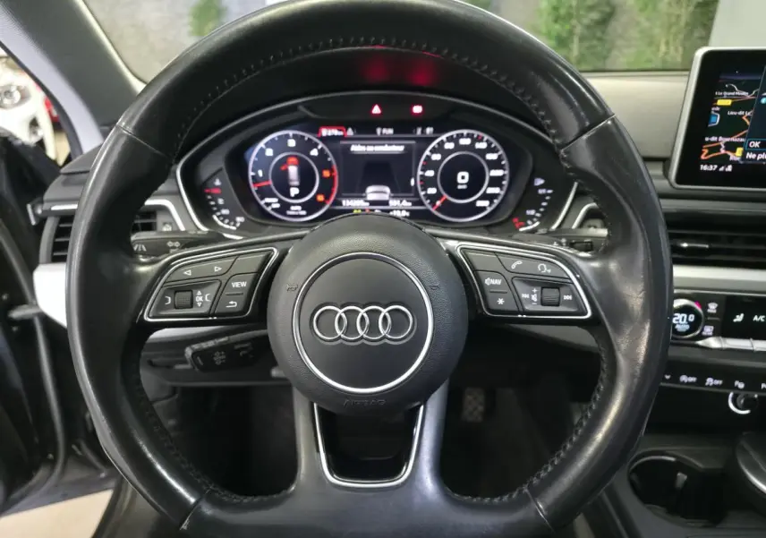Vue rapprochée du volant en cuir noir d'une Audi A4 Allroad 2017 avec tableau de bord numérique et écran de navigation.