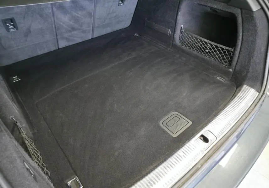 Coffre spacieux de l'Audi A4 Allroad gris, vue plongeante montrant tapis noir et filet de rangement latéral.