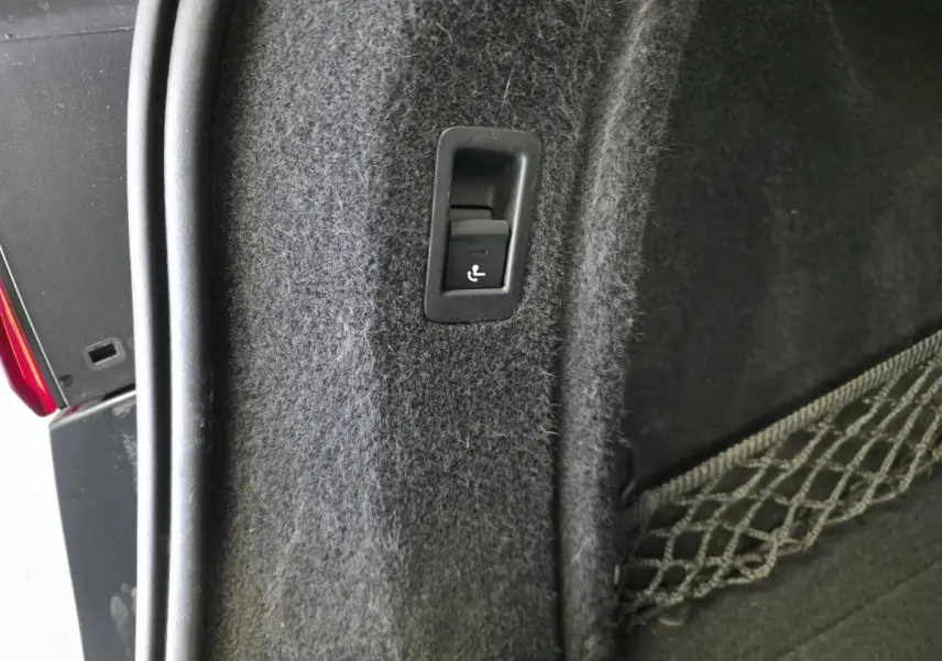 Détail du bouton de rabattement de siège dans le coffre d'un Audi A4 Allroad gris, avec filet de rangement visible.