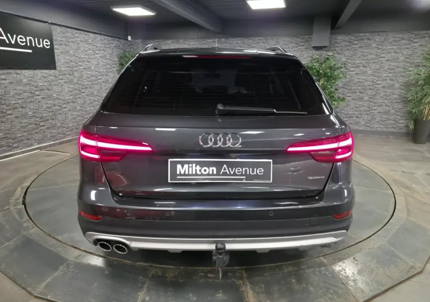 Vue arrière d'une Audi A4 Allroad Quattro gris métallisé avec feux allumés et crochet d'attelage visible.