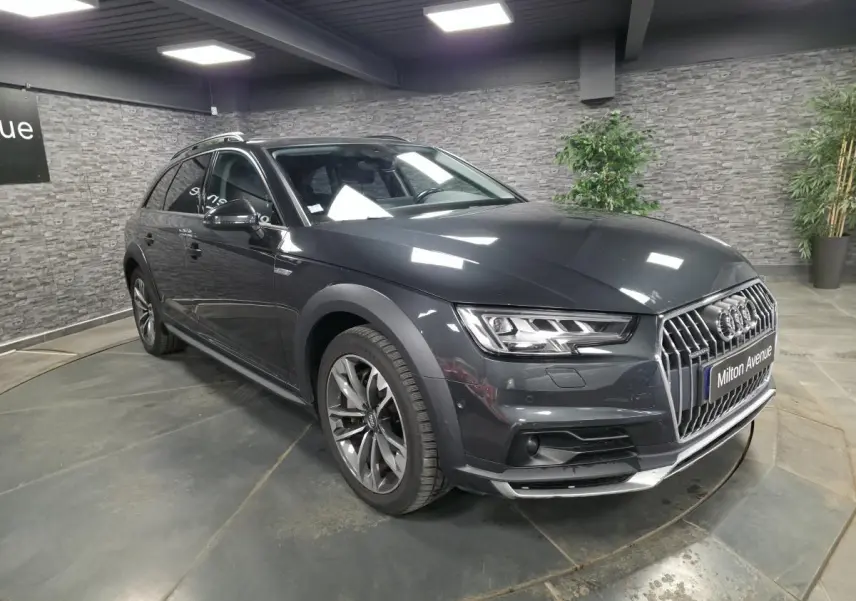 Audi A4 Allroad gris métallisé vue 3/4 avant droit en intérieur avec calandre chromée et jantes 5 branches doubles.