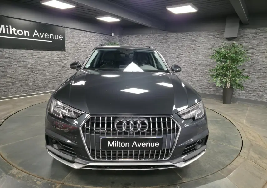 Audi A4 Allroad Quattro gris vue de face dans un showroom avec éclairage et décor mural en pierre grise.