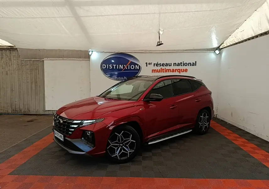 Hyundai Tucson rouge vue 3/4 avant droit en intérieur, avec jantes alliage noires et toit noir.