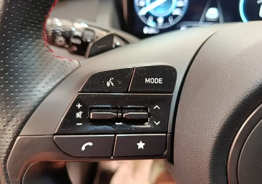 Gros plan sur les commandes multifonctions noires du volant cuir perforé côté gauche du Hyundai Tucson rouge 2022.