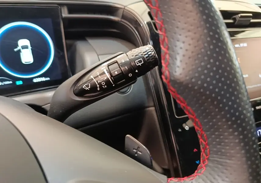 Gros plan sur la commande d’essuie-glace à gauche du volant perforé noir avec surpiqûres rouges du Hyundai Tucson rouge 2022.