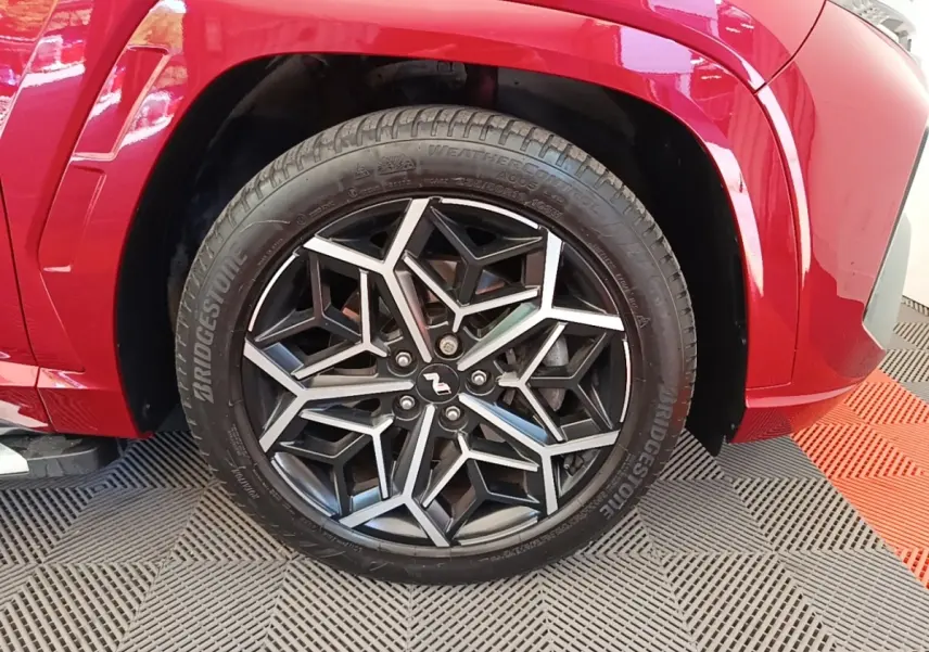 Gros plan sur la roue avant gauche du Hyundai Tucson rouge, avec jante alliage noire et argentée au design géométrique N Line.