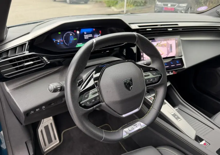 Vue intérieure du poste de conduite de la Peugeot 408 PHEV 225 GT bleu, avec volant multifonction et écran tactile central.