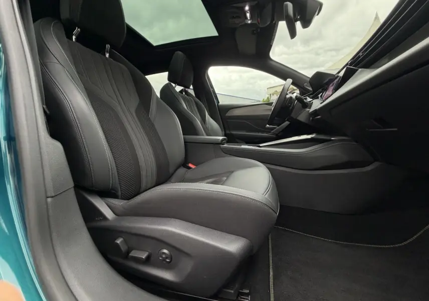 Vue intérieure côté conducteur de la Peugeot 408 PHEV 225 GT bleu, sièges cuir noirs et toit panoramique visible.