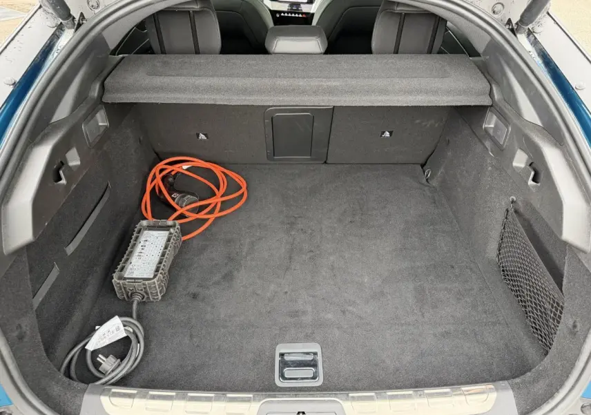 Coffre ouvert d’une Peugeot 408 PHEV 225 GT bleu 2023, montrant la moquette noire et le câble de recharge orange.