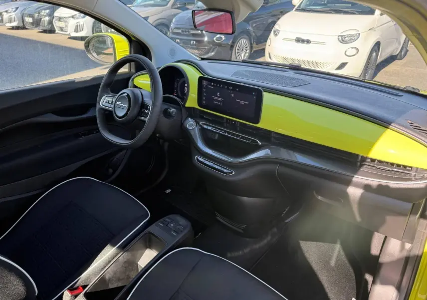 Vue intérieure côté conducteur de la Fiat 500 électrique jaune, tableau de bord avec écran tactile et volant multifonction.
