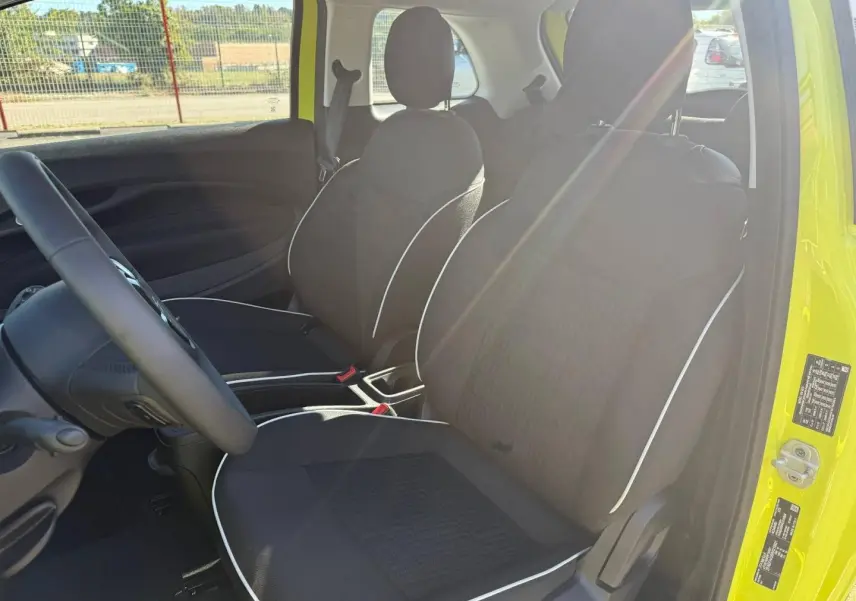Vue intérieure côté conducteur de la Fiat 500 e 95ch MY24 jaune, sièges noirs avec surpiqûres blanches et volant multifonction.
