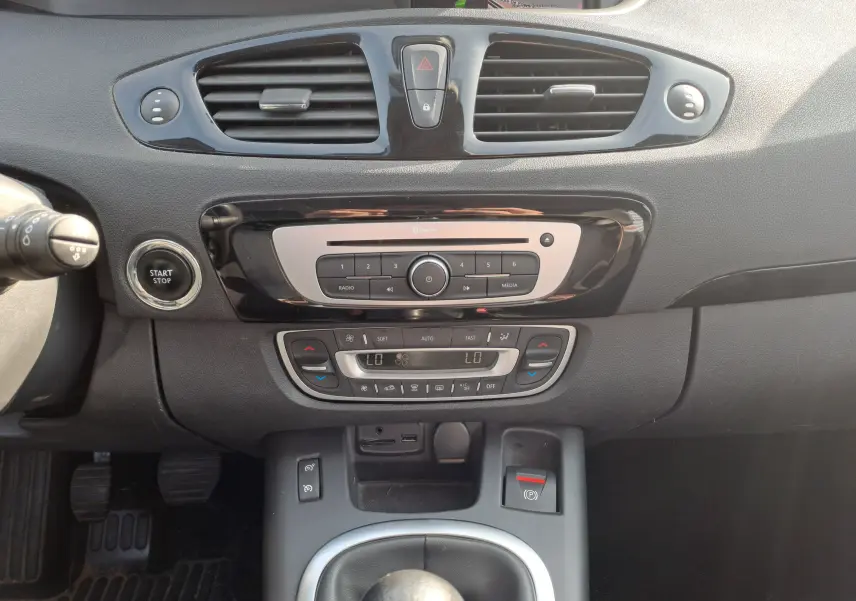 Vue rapprochée du tableau de bord noir du Renault Scenic III 2016, montrant la console centrale avec commandes climatisation et bouton start-stop.