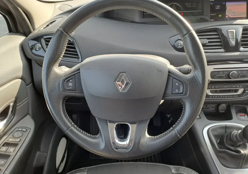 Vue rapprochée du volant en cuir noir avec logo Renault, tableau de bord et levier de vitesses d'une Renault Scenic III gris 2016.