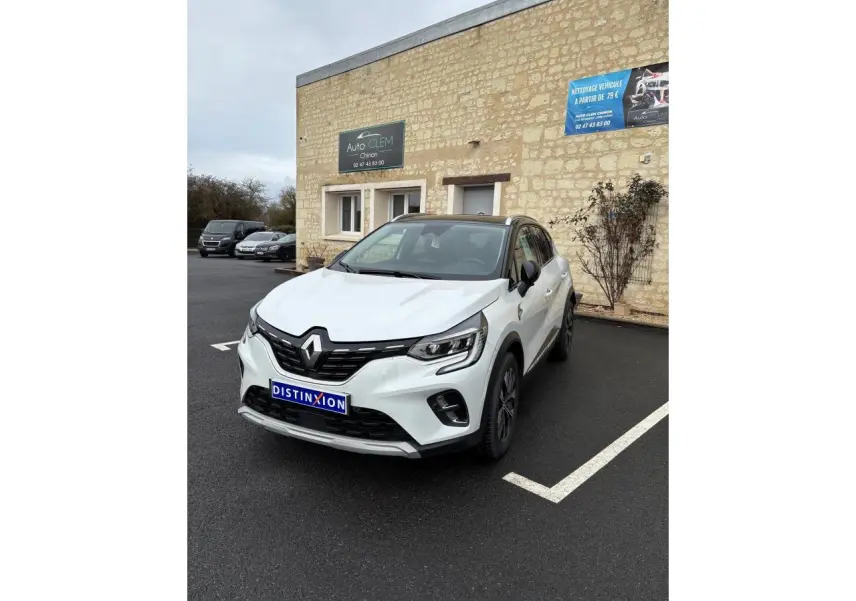 Renault Captur blanc en 3/4 avant droit, avec toit noir et calandre noire brillante, stationné devant un mur en pierre.