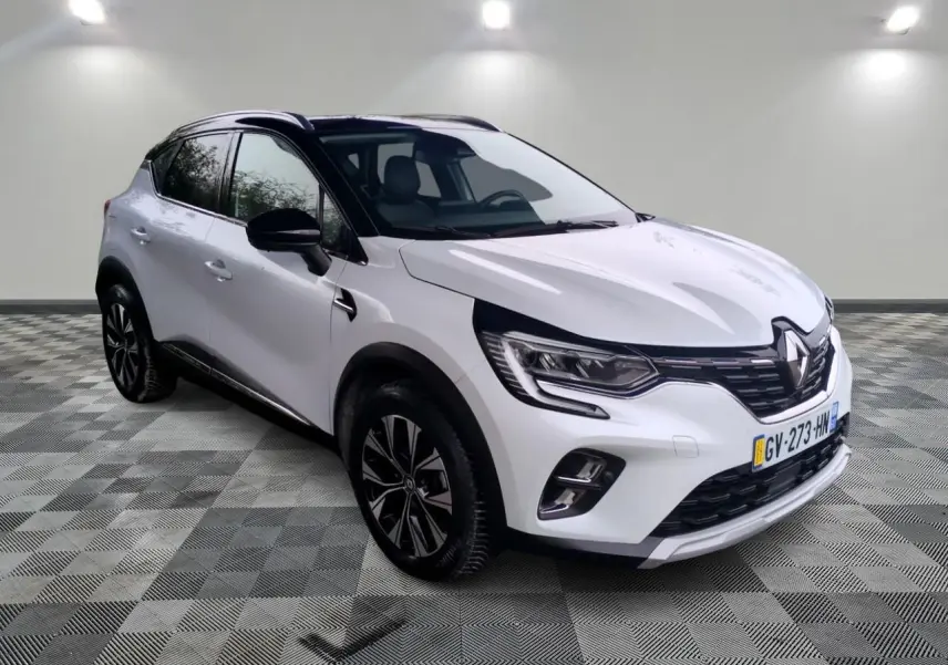 Renault Captur blanc en 3/4 avant droit, avec toit noir et jantes alliage bicolores sur fond neutre intérieur.