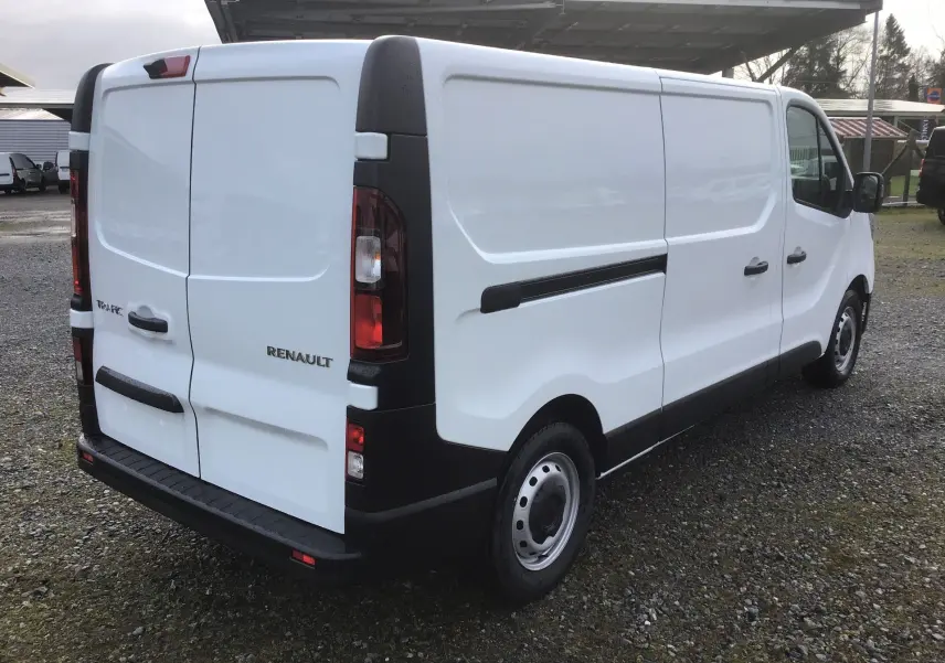 Vue 3/4 arrière droite d'un Renault Trafic Fourgon blanc 2025 avec portes arrière battantes et protections noires.