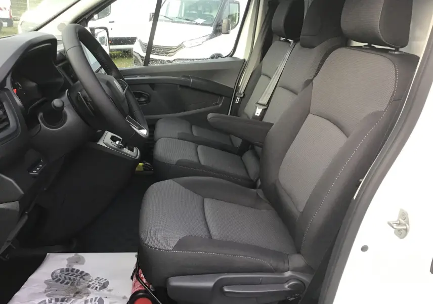 Vue intérieure côté conducteur du Renault Trafic Fourgon blanc 2025, montrant les sièges gris et le volant avec boîte automatique.