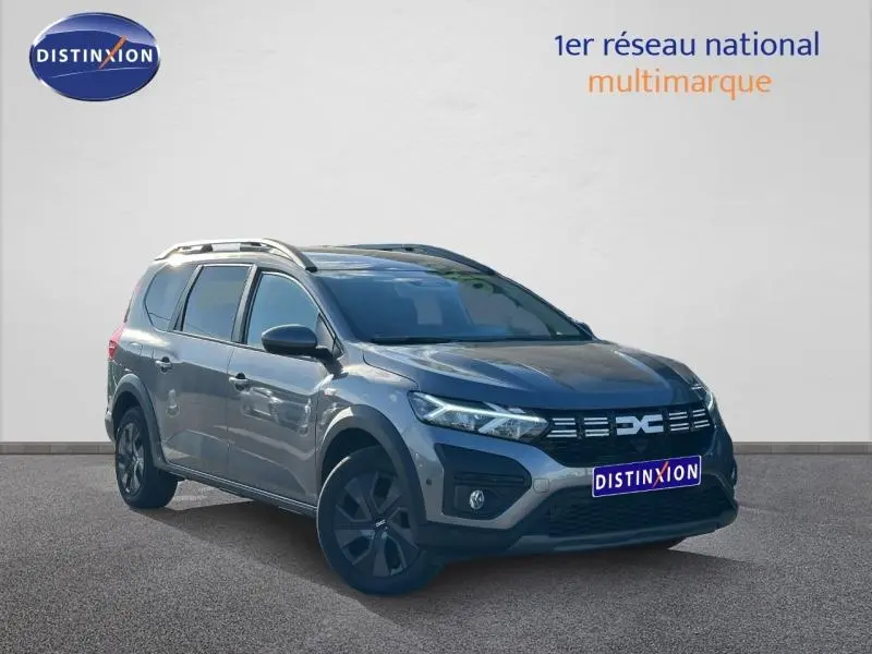Dacia Jogger 2025 gris schiste métallisé, vue 3/4 avant droit, avec barres de toit et jantes noires distinctives.