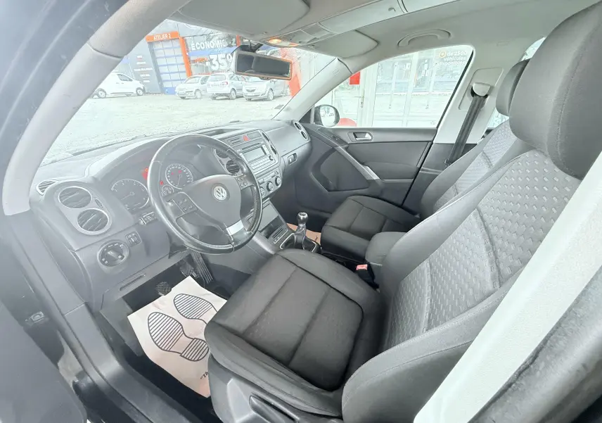 Vue intérieure côté conducteur du Volkswagen Tiguan noir de 2007, montrant le volant, les sièges en tissu noir et la console centrale.