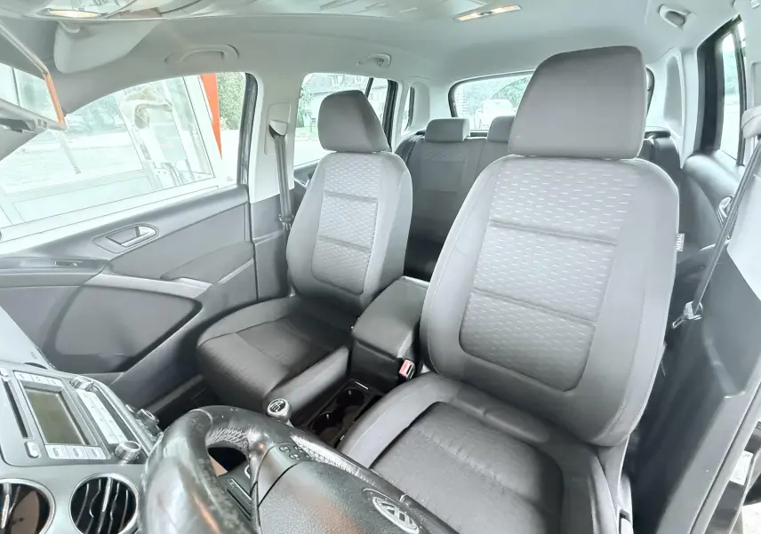 Vue intérieure avant du Volkswagen Tiguan noir 2007, sièges tissu gris et volant multifonctions visible.