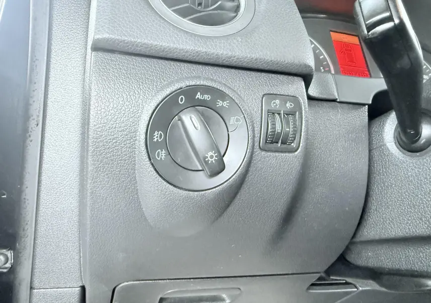 Gros plan sur le tableau de bord noir du Volkswagen Tiguan 2007, montrant la molette des phares et les réglages d’éclairage.