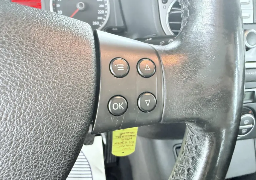 Gros plan sur les commandes à gauche du volant noir du Volkswagen Tiguan 2007, avec tableau de bord en arrière-plan.