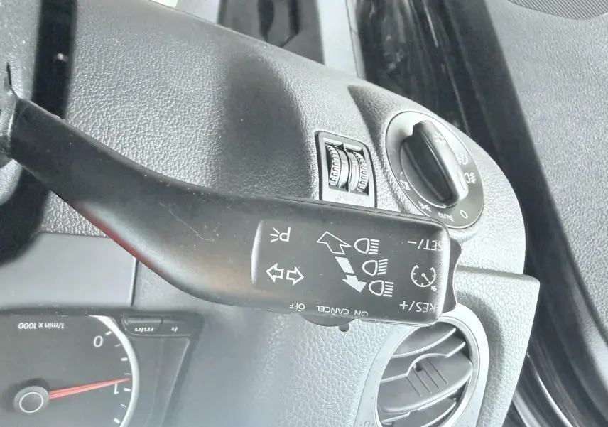 Gros plan sur la commande de clignotants et phares à gauche du tableau de bord d’un Volkswagen Tiguan noir.
