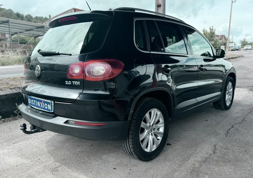 Vue 3/4 arrière droite d'un Volkswagen Tiguan noir avec attelage et jantes alliage sur route urbaine.