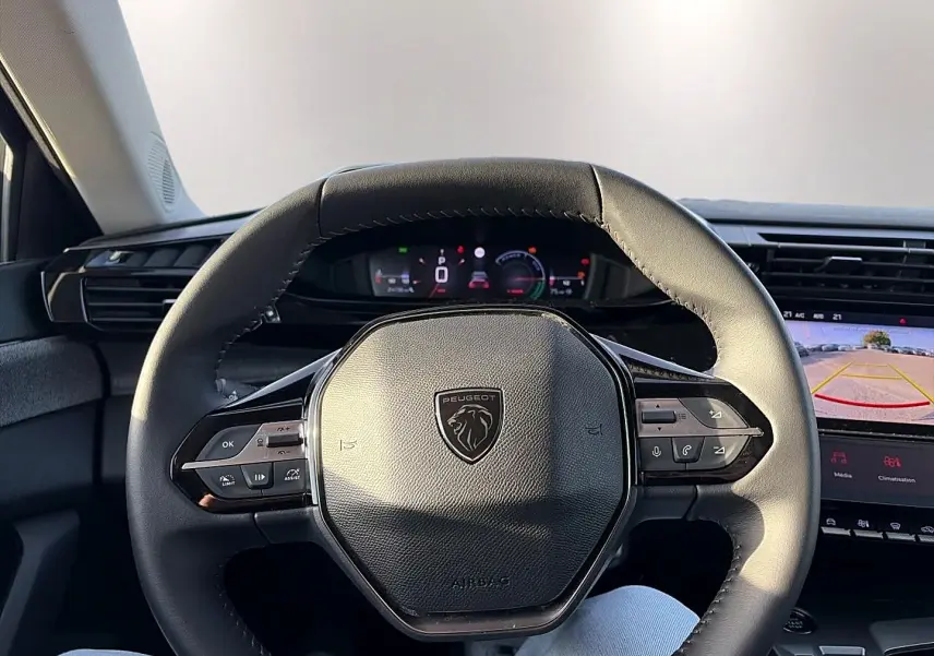 Vue intérieure centrée sur le volant cuir noir de la Peugeot 408 Hybrid 145 avec tableau de bord digital et écran tactile.