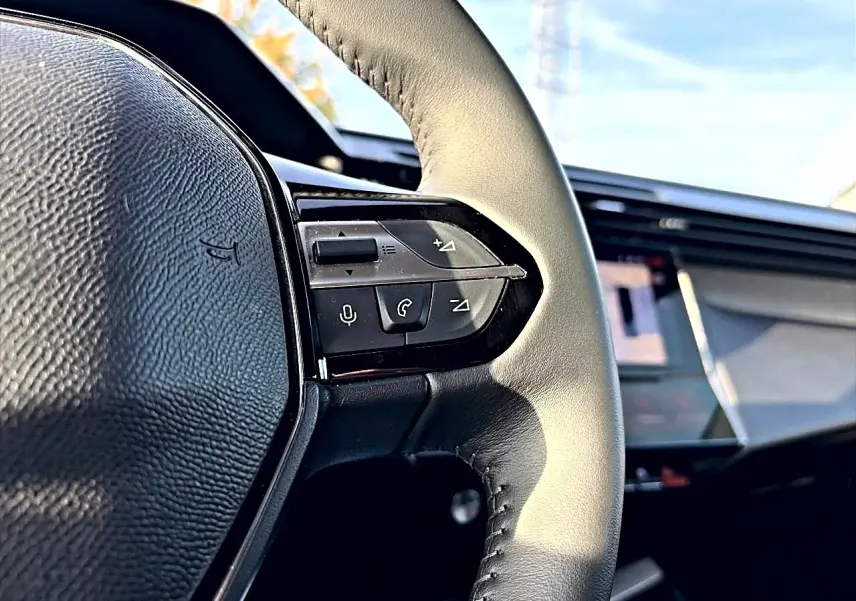 Gros plan sur le volant cuir noir de la Peugeot 408 Hybrid 145 allure e-dcs6 avec commandes vocales et téléphone intégrées.