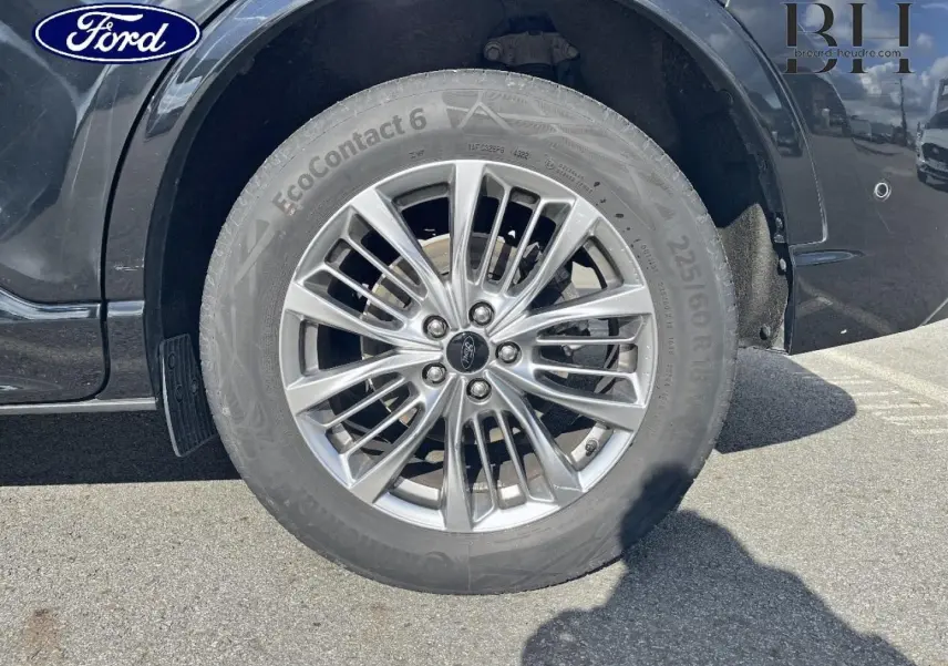 Gros plan sur la roue avant droite du Ford Kuga noir Agate Métallisée avec jante alu multi-branches et logo Ford central.