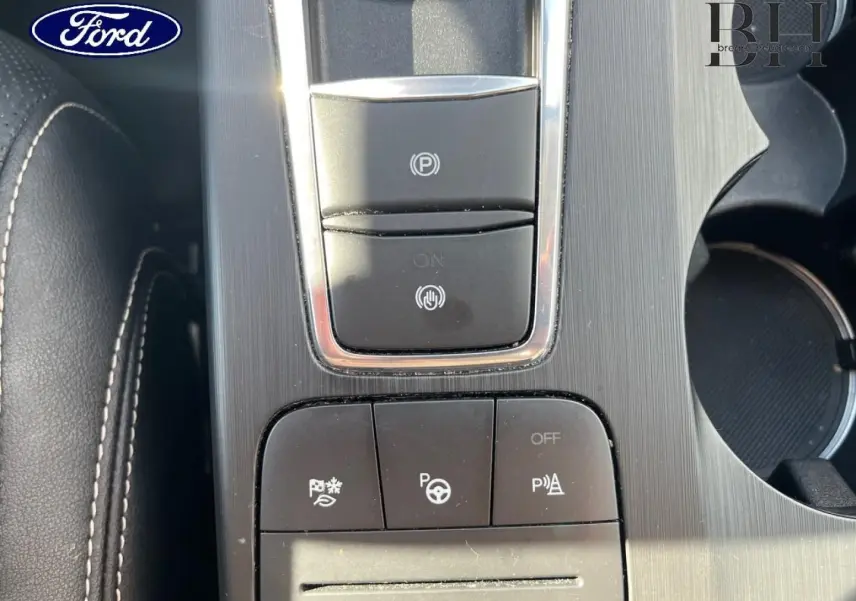 Gros plan sur la console centrale du Ford Kuga noir Agate, montrant les boutons du frein à main électronique et du pack assistance.