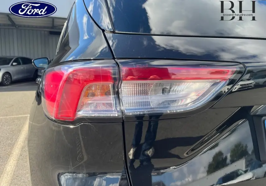 Gros plan sur le feu arrière gauche du Ford Kuga 2023 noir Agate Métallisée, avec reflet du ciel et de l'environnement.
