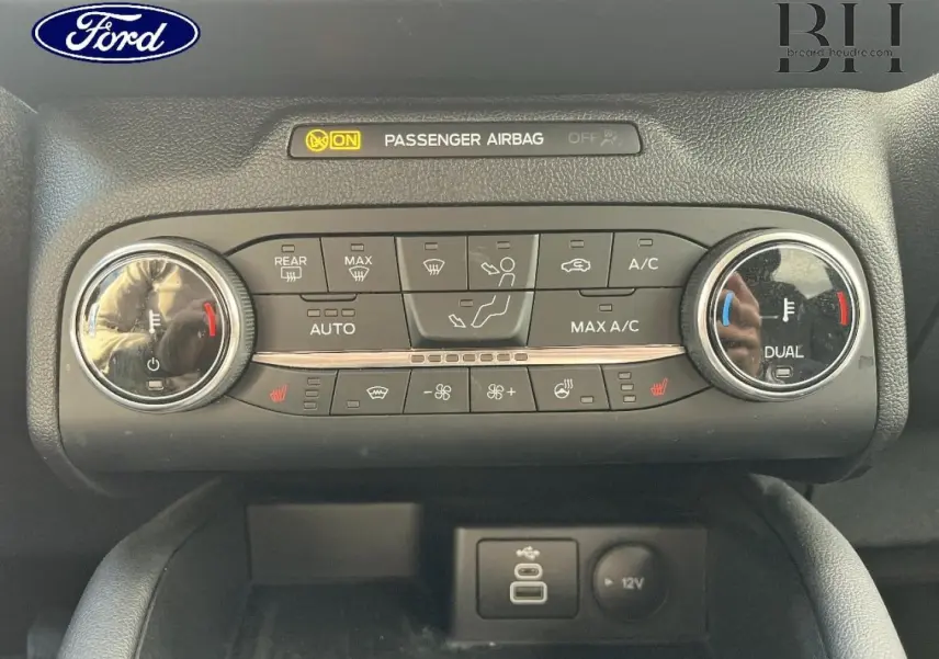 Vue rapprochée de la console centrale du Ford Kuga 2023, avec commandes climatisation bi-zone et ports USB et 12V.