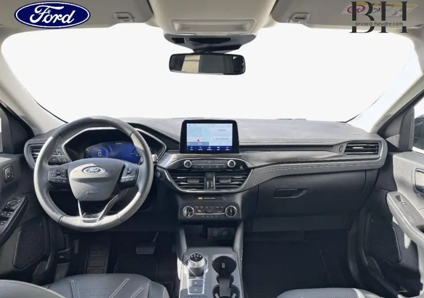 Vue intérieure avant du Ford Kuga 2023, tableau de bord noir avec écran tactile central et volant cuir multifonction.