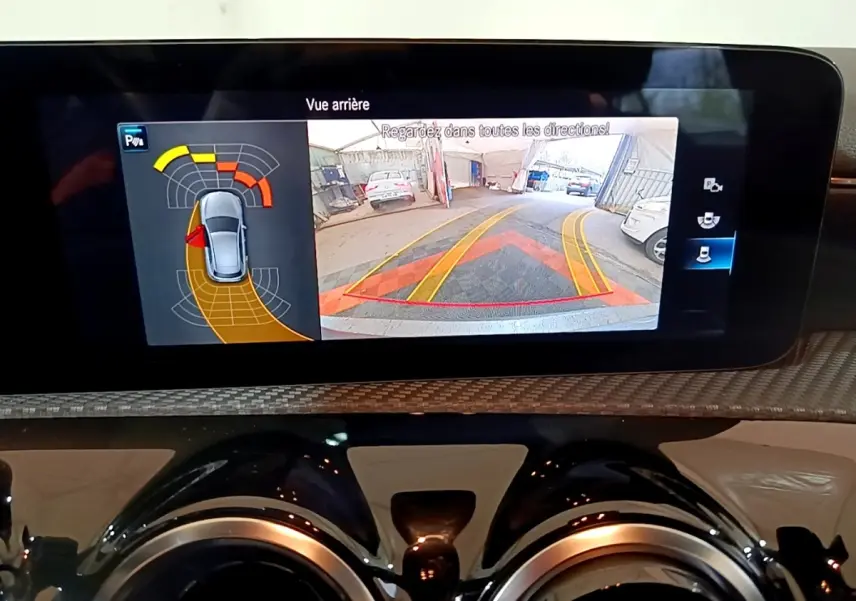 Écran tactile intérieur montrant l’aide au stationnement arrière avec vue caméra et capteurs sur Mercedes Classe A gris foncé.